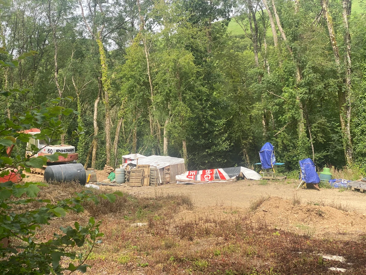 Excavator marked Poclain 60 beside a cleared working area, tank, materials and covered equipment.