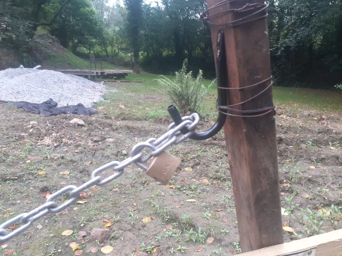 Close view of a metal chain resting on an open hook, with a padlock attached to chain links.